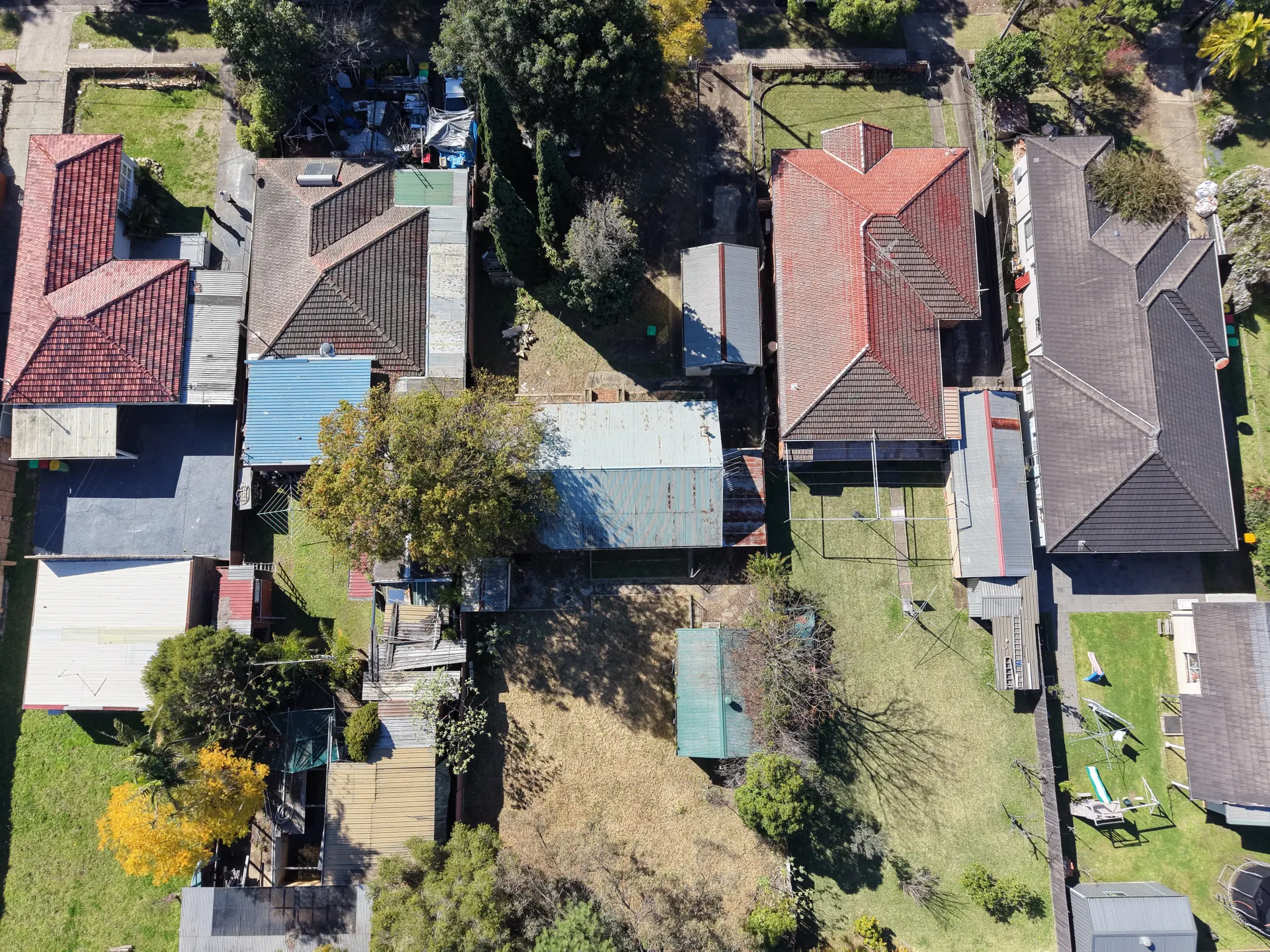 Directly overhead view of a long rectangular building with a corrugated metal roof, the open yard behind it and a small outbuilding.